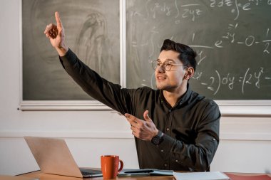 Masa başında oturan, parmak havada işaret ve denklemler matematik sınıfında açıklayan erkek öğretmen