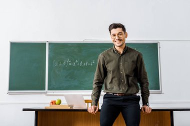 kameraya bakarak ve resepsiyon sınıfta yakın duran formal giyim gülümseyen erkek öğretmen
