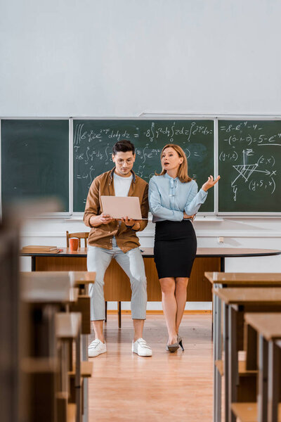 selective focus of male student and female teacher using laptop during lesson in classroom