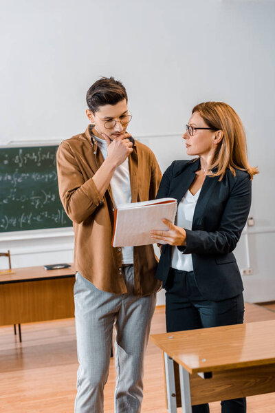female teacher helping pensive male student with assignment during lesson in classroom