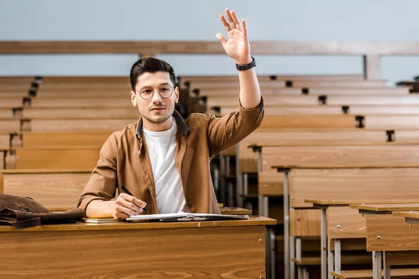 Focused Male Student Glasses Sitting Desk Raising Hand Lesson Classroom — Stock Photo, Image