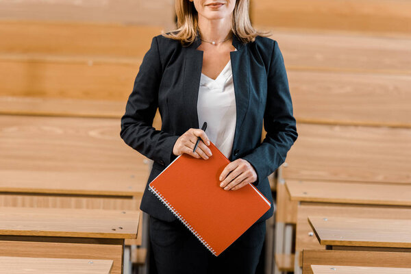 cropped view of female university professor holding journal in classroom