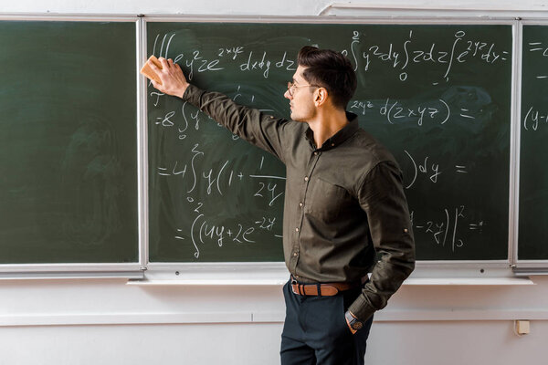 male teacher in formal wear wiping mathematical equations with sponge in classroom