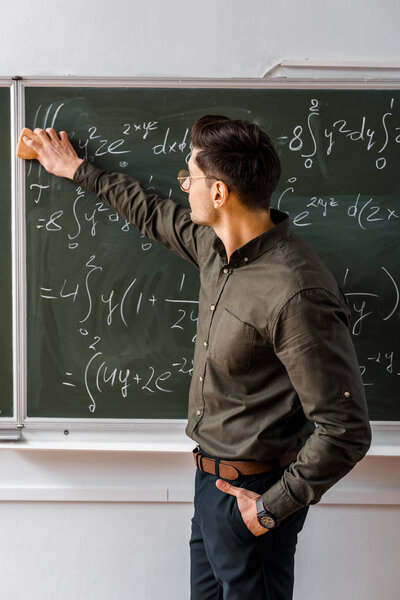 male teacher wiping mathematical equations with sponge from chalkboard in classroom