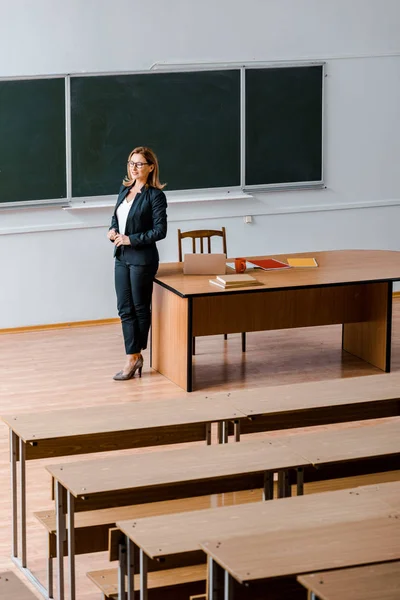 female university professor in formal wear standing near chalkboard in classroom