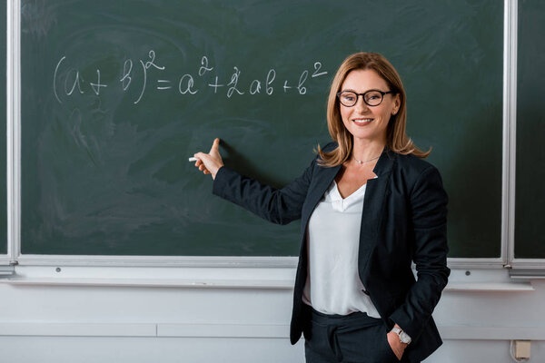 female teacher pointing with finger at mathematical equation on chalkboard in class
