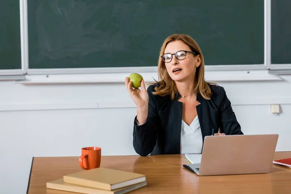 Lehrerin Sitzt Computertisch Und Hält Apfel Klassenzimmer — Stockfoto