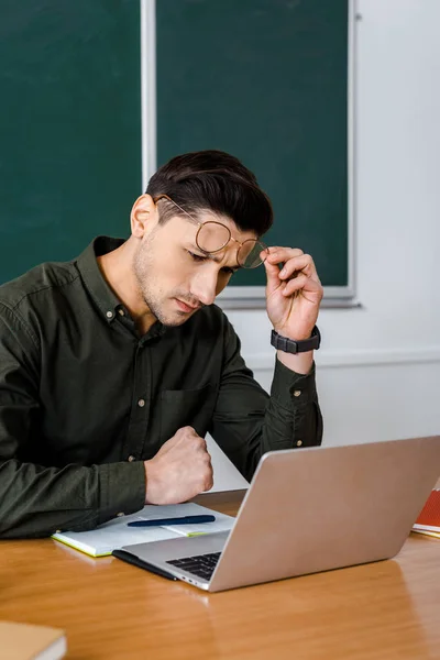在教室的桌子上 用笔记本电脑集中的男老师戴眼镜 — 图库照片