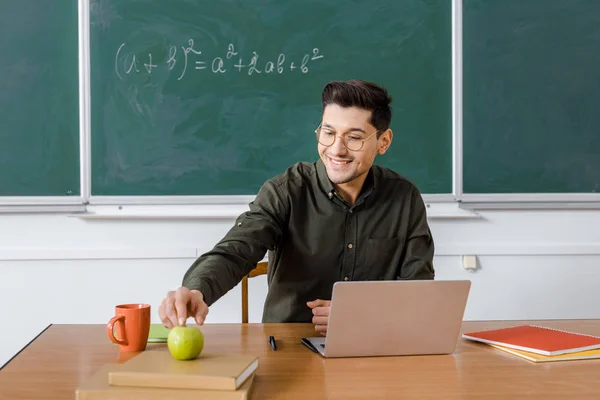 Smiling Male Teacher Glasses Sitting Computer Desk Reaching Apple Classroom — Stock Photo, Image
