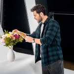 Jeune photographe souriant arrangeant des fleurs en studio photo
