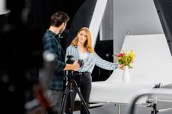 selective focus of young photographers looking at each other while shooting flowers in studio 