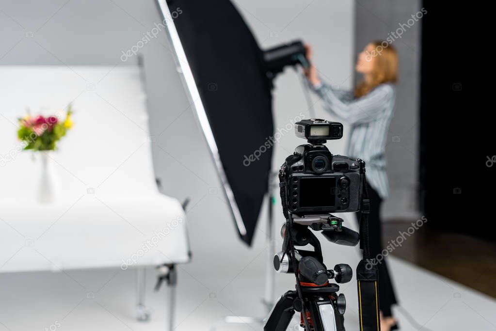 close-up view of photo camera and young woman working with lighting equipment in studio