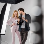 Selective focus of smiling young photographer and model checking photos on camera in studio