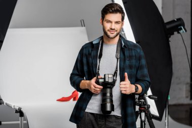 yakışıklı gülümseyen genç fotoğrafçı kamera ve gösteren başparmak studio gidiyor