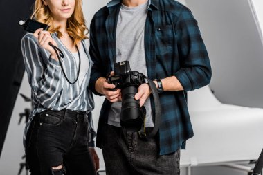 cropped shot of young photographers holding camera and light meter in studio clipart