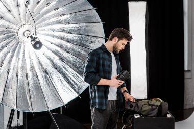 sırt çantasında fotoğraf stüdyosu bakarak ve objektif tutan yakışıklı genç fotoğrafçı