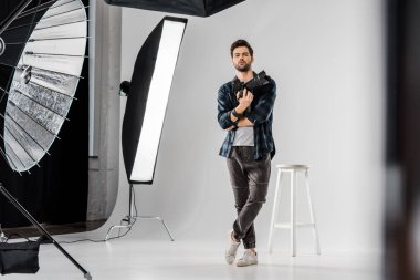 kendine güvenen genç fotoğrafçı profesyonel kamera tutarak ve kamera fotoğraf Studio bakarak görünümünü tam uzunlukta 