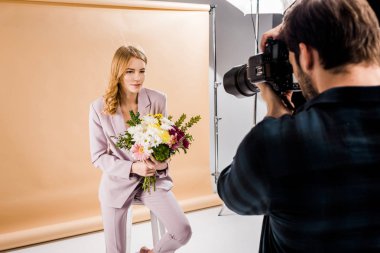 photographer shooting beautiful young woman posing with flowers in studio clipart
