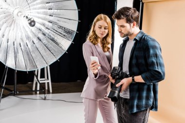 Kamera ve fotoğraf stüdyosunda smartphone kullanarak güzel modeli ile genç fotoğrafçı 