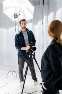 fotoğraf makinesi ile ayakta ve güzel fotoğraf stüdyosu modelinde bakarak yakışıklı genç fotoğrafçı