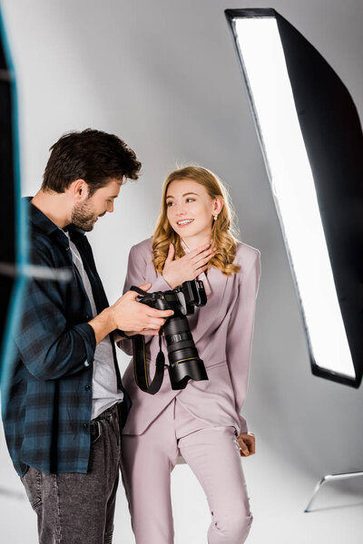 smiling young photographer and beautiful model checking photos on camera in studio 