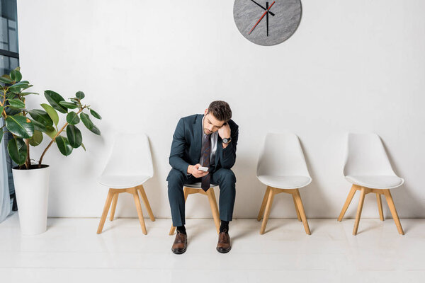 bored young businessman using smartphone while waiting in queue