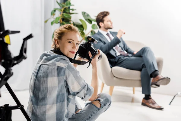 Joven Fotógrafa Sonriendo Cámara Mientras Fotografía Apuesto Hombre Negocios Estudio —  Fotos de Stock