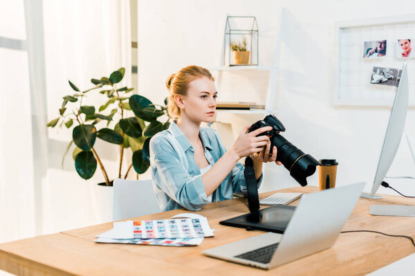 beautiful young photographer holding camera and retouching photos in office