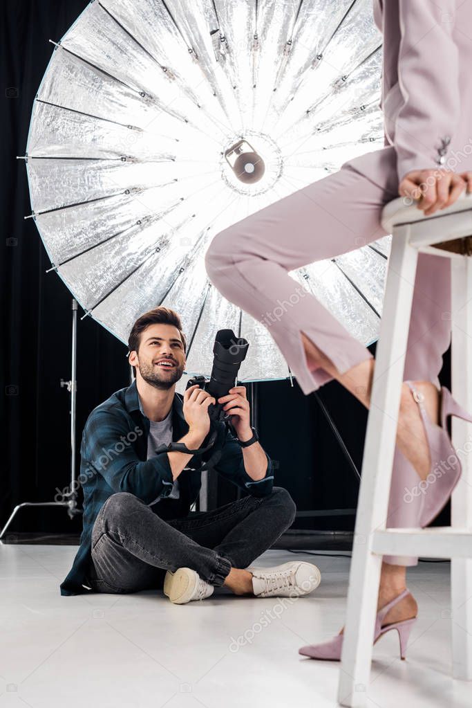 cropped shot of smiling photographer sitting and photographing stylish model in studio  