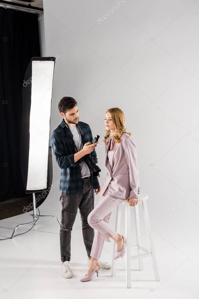 young photographer holding light meter and working with beautiful female model in studio