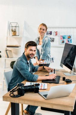 office Fotoğraflarda rötuş yaparken kameraya gülümseyen genç profesyonel fotoğrafçılar 