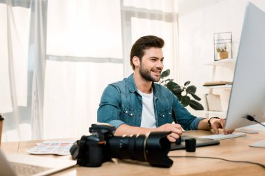 Masaüstü bilgisayar kullanarak ve işyerinde fotoğraf rötuş gülümseyen genç fotoğrafçı