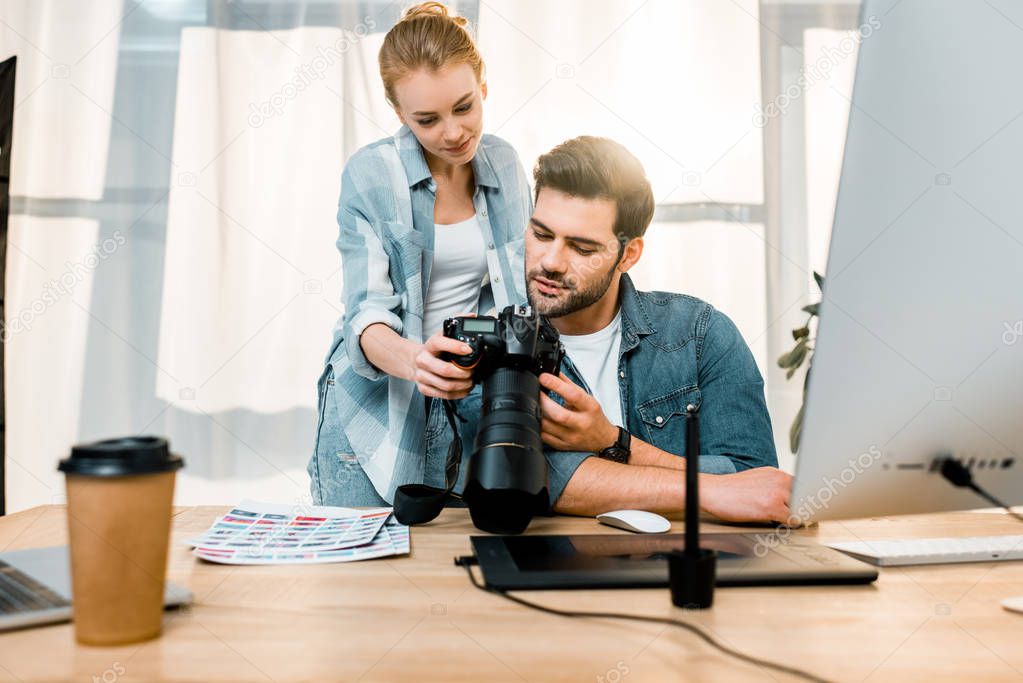 professional smiling young photographers using photo camera together in office