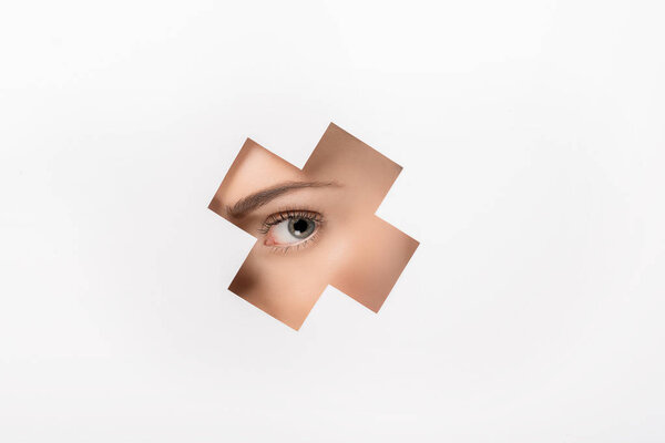 partial view of beautiful girl looking at camera through cross shaped hole on white 