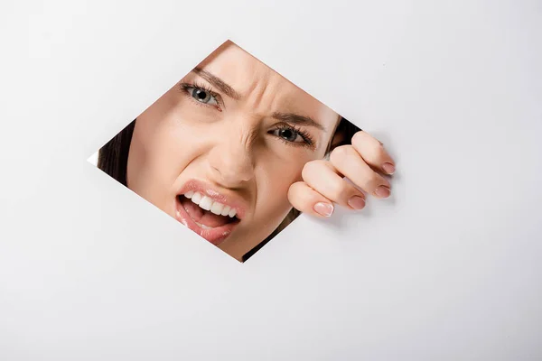 Arrabbiato Giovane Donna Guardando Fotocamera Attraverso Buco Sul Bianco — Foto Stock