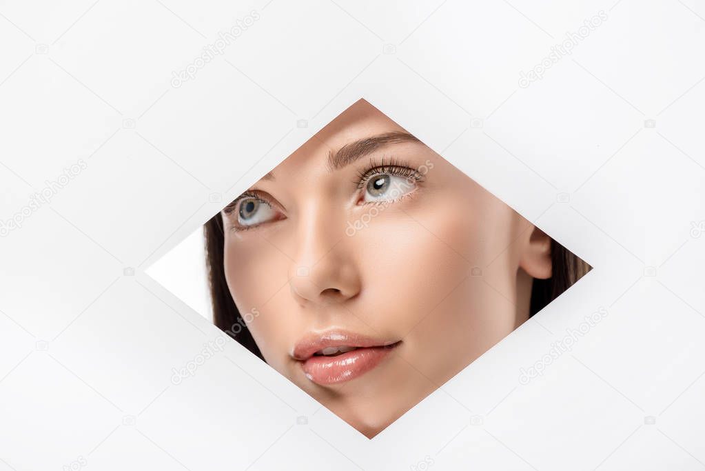 thoughtful young woman looking away through rhombus shaped hole on white  