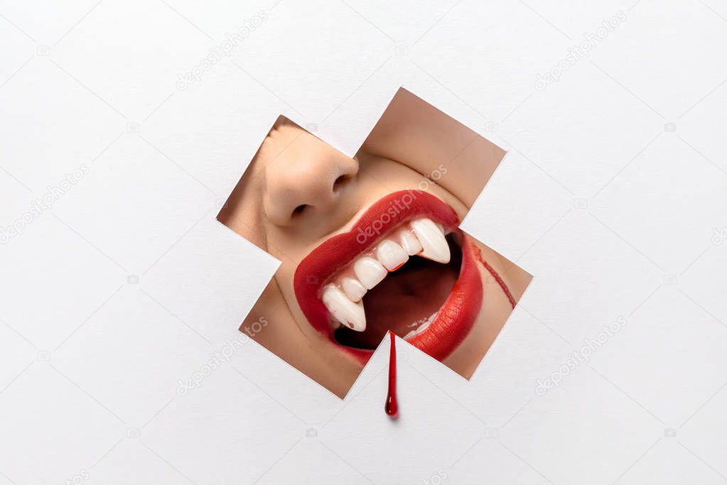 cropped shot of woman showing vampire teeth through cross shaped hole on white 