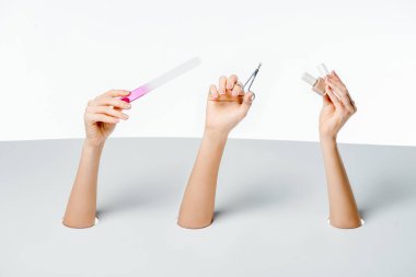 cropped shot of women holding nail file, scissors and polishes through holes on white clipart