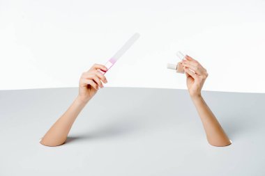 cropped shot of woman holding nail file and polishes through holes on white  clipart