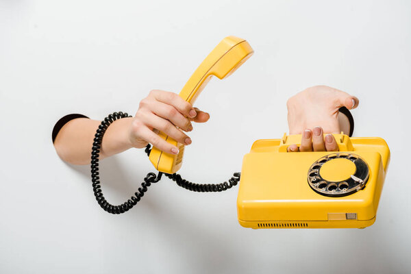 cropped image of woman holding retro yellow stationary telephone through holes on white