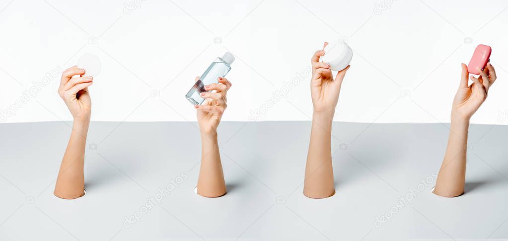 cropped shot of women holding soap, cotton pad, lotion and cream through holes on white