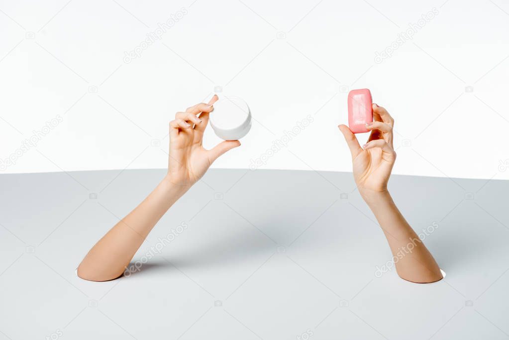 cropped shot of woman holding soap and cream through holes on white 