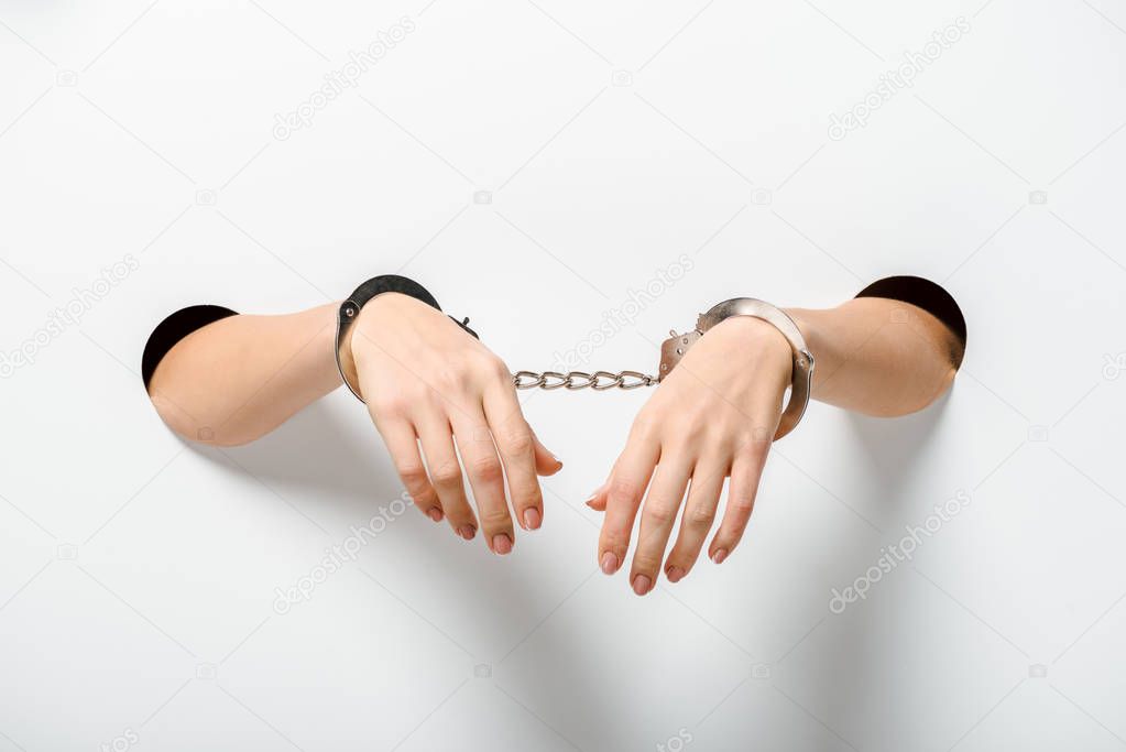 cropped image of woman in handcuffs holding hands through holes on white