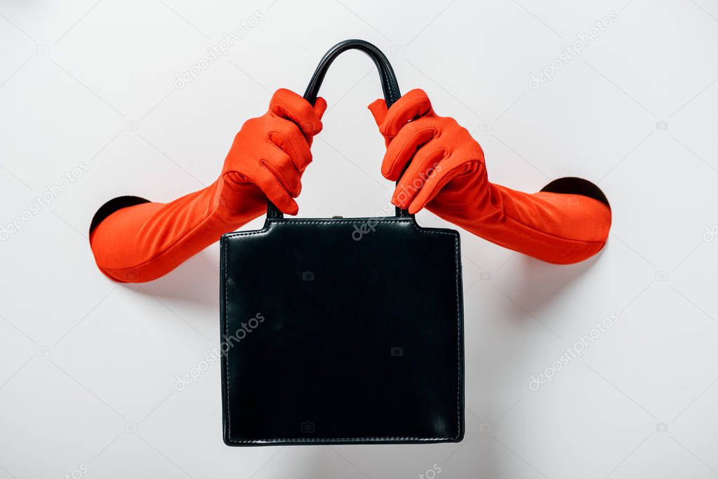 cropped image of woman in red gloves holding black handbag through holes on white
