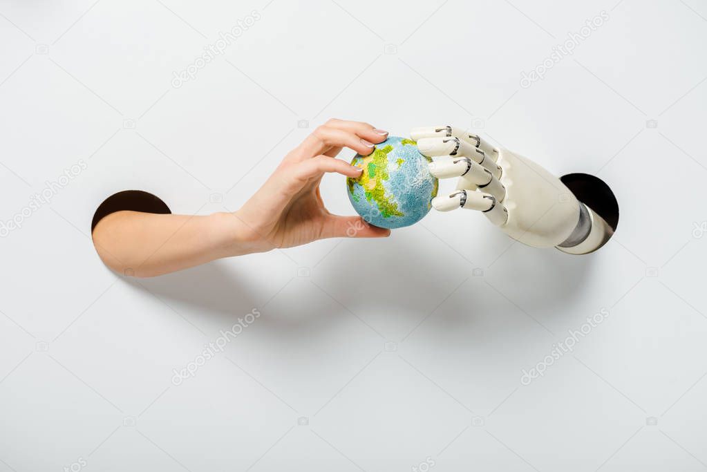 cropped image of woman and robot holding earth model through holes on white environment