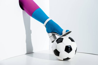 cropped image of woman putting leg in violet tights, blue sock and white high heel on football ball through hole on white clipart