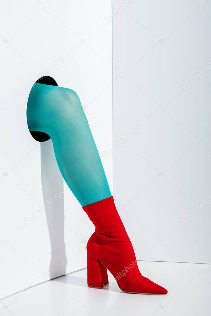 cropped image of girl showing leg in turquoise tights and red shoe in hole on white