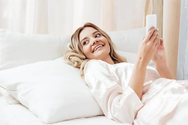 Χαρούμενη Όμορφο Κορίτσι Χρησιμοποιώντας Smartphone Στο Κρεβάτι Κατά Διάρκεια Του — Δωρεάν Φωτογραφία