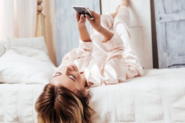 Smartphone yatakta evde sabah zaman sırasında kullanan gülümseyen kız