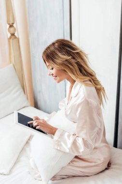 evde sabah zaman sırasında yatakta boş ekran dijital tablet kullanarak Pijama içinde gülümseyen sarışın kadın